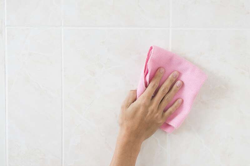 hand using pink rag to wipe down tiled wall